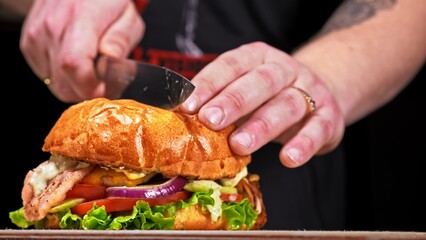 Cut craft burger is cooking on black background. Consist: sauce, lettuce, tomato, red onion, cucumber, cheese, bacon, air bun and breast of chicken. Not made ideal. Looks real, loving hand made.