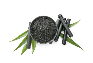 Bowl with activated carbon powder and black bamboo sticks on white background