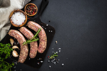 Bratwurst or sausages on dark cutting board with rosemary and spices. Top view with copy space.