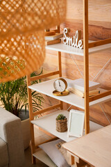 Shelving unit with books, alarm clock and frame near wooden wall