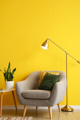 Golden standard lamp with armchair and table near yellow wall