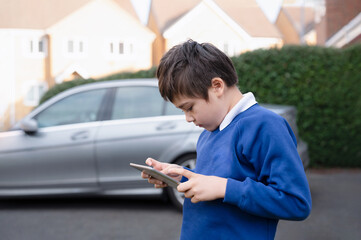 Happy Child boy holding tablet pc standing outside waiting for School bus, Portrait Kid playing...