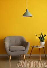 Comfortable armchair with table and lamp hanging near yellow wall