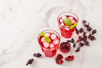 two glasses with tonic vitamin cold tea from hibiscuss rose petals with pieces of ice and mint on a marble background.