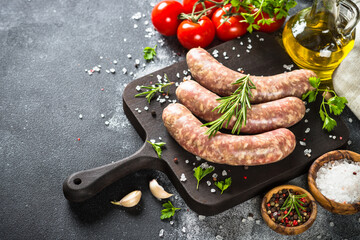 Bratwurst or sausages on cutting board with spices and herbs at dark table. Natural meat sausages.