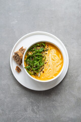 Cream of carrot soup in a white bowl. Carrot soup served in a bowl on a gray background. Bowl of carrot soup with arugula leaves on concrete table
