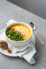 Cream of carrot soup in a white bowl. Carrot soup served in a bowl on a gray background. Bowl of carrot soup with arugula leaves on concrete table