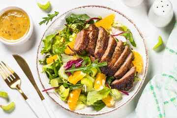 Salad with baked duck, green salad mix and oranges and honey mustard dressing. Healthy food, diet meal. Top view at white marble table.