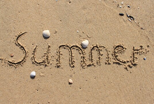 on the beach is carved with letters in the smooth sand the writing SUMMER