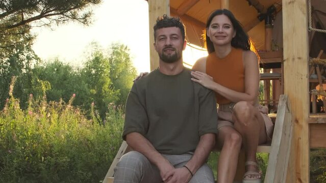 Portrait of young Biracial wife and husband sitting on stairs outside glamping, posing, looking and smiling on camera on sunny day
