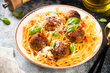 Pasta with Meatballs in tomato sauce, basil and parmesan on light stone table.
