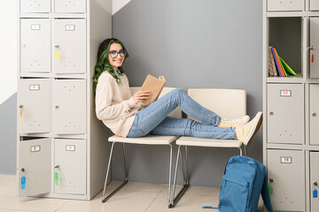 Beautiful female student reading book while sitting near locker at the university