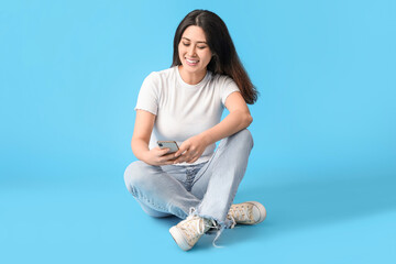 Beautiful young Asian woman with mobile phone on blue background