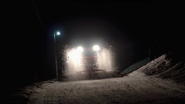 Snowcat ratrack with snowplow preparing the ski slope, driving through the deep snow piste in the ski resort. Heavy machinery mountain equipment at night