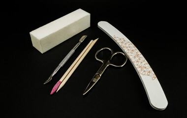 Manicure and pedicure tools on black background. Silver scissors, nail file, buffer block, cuticle pusher and orange wood sticks.