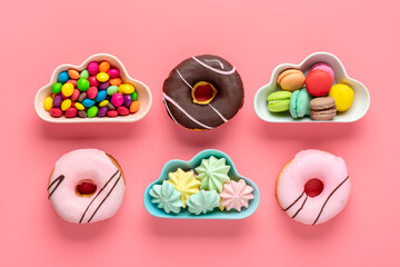 sweets and meringues in bowl in shape of cloud, chocolate with colorful topping and pink donut isolated on pink background Flat lay Top View Knolling Unhealthy and tasty food concept