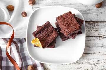 Plate with pieces of delicious chocolate brownie on white wooden background