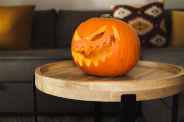 Carved Halloween pumpkin, jack lantern (Jack-o'-lantern). Spooky laughing, scary head on a small table in a home living room, with a couch in the background. - Powered by Adobe