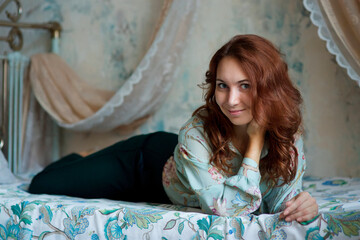 A girl with red hair is lying on the bed.