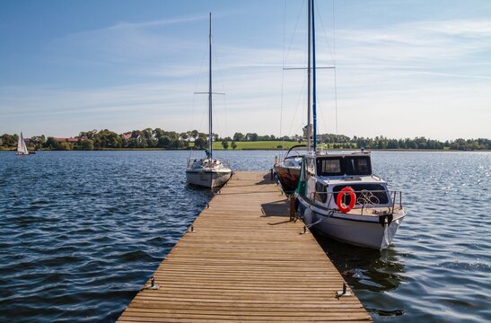 Fototapeta Peaceful blue lake with small wooden pier and private sailing boats or yachts.