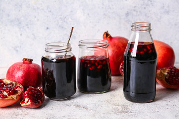 Jars of pomegranate molasses and fresh fruits on light background