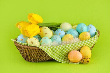 Wicker basket of painted Easter eggs and flowers on green background