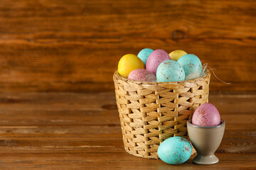 Wicker basket and cup with painted Easter eggs on wooden background