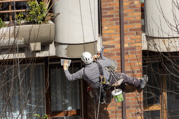 trabajador colgado de una cuerda trabajando en altura reparando la fachada de un edificio o...