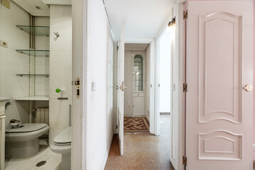 Corridor of a residential house with cork floors, access door to a toilet and wood and glass showcase in the background