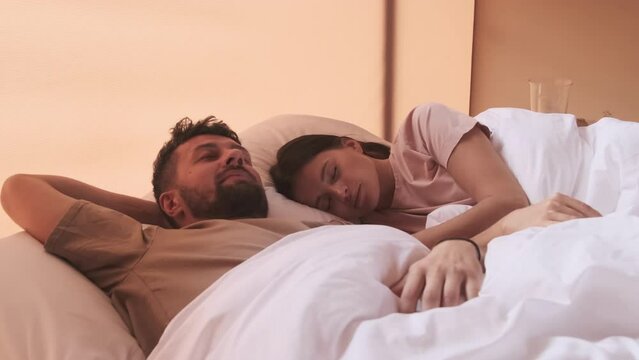 Young dark-haired Biracial woman and bearded husband sleeping in bed in hotel room in morning