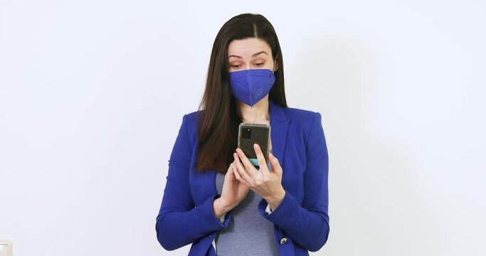 Beautiful woman with a blue jacket looks at her smartphone and then takes off her FFP2 mask. Without a mask in the office. Businesswoman with ffp2 mask. Woman looking forward to her office job during 