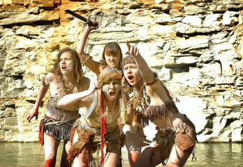 A group of woman dress up as a Neanderthal warriors. 
Their bodies and faces are covered with mud...