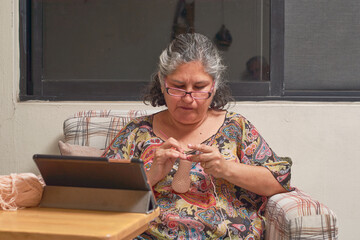 Fototapeta na wymiar Middle-aged woman takes virtual knitting class on her tablet.