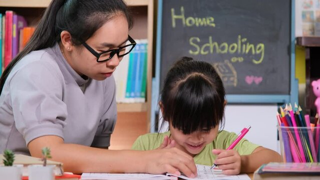 Asian little girl studies at home during quarantine with her mother.  Mother helping little daughter with homework at home. Home schooling.