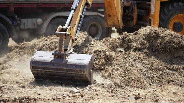 Close up of industrial excavator loading soil material on a highway construction site into a dumper truck, slow motion