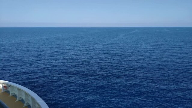 View of the open sea horizon from a cruise. Front of the cruise can be seen on the side. It's a lower deck terrace with wooden look floor and metal veranda painted white.