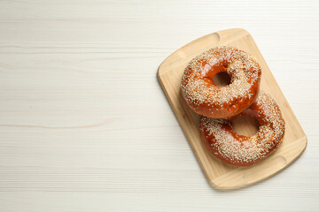 Delicious fresh bagels with sesame seeds on white wooden table, top view. Space for text