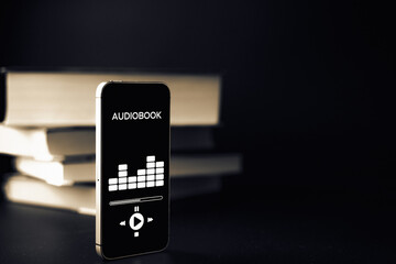 Audiobook education. Smartphone screen with audiobook application on paper books black background....