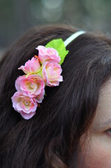 Obraz na płótnie Canvas A wreath of pink flowers in the girl's black hair. Hairpin with artificial flowers