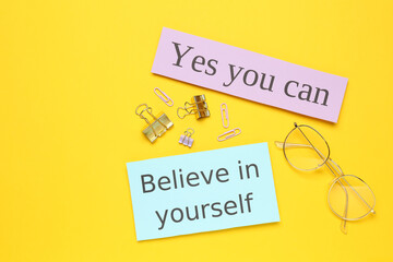 Notes with motivational quotes, glasses and office stationery on yellow background, flat lay
