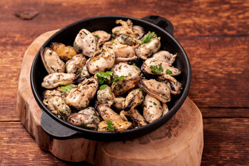 Peeled mussels in sauce on a dark wooden background.