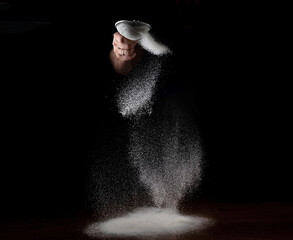 Flour flies through a sieve on a black background. A man sifts flour for cooking. Culinary theme.