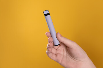 Woman holding electronic cigarette on orange background, closeup