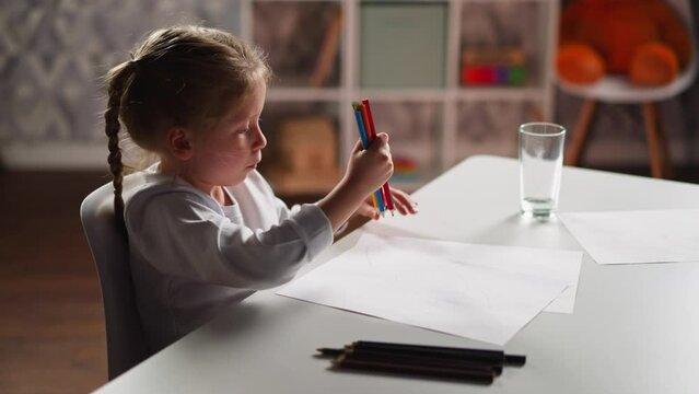 Little artist gathers crayons in bunch to draw at table