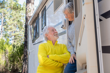 Carefree attractive senior couple standing out of their camper van motor home talking and smiling...