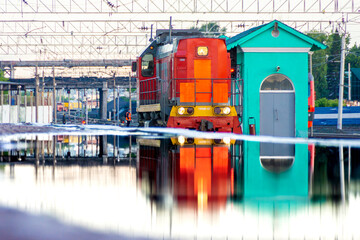 red diesel locomotive is reflected in huge puddle on platform formed from mistakes made in designing passenger platform