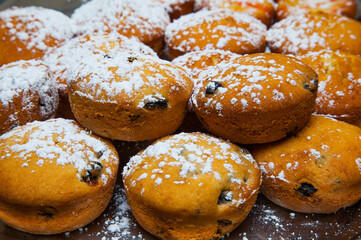 Ready baked muffins with raisins sprinkled with powdered sugar on a tray close-up.