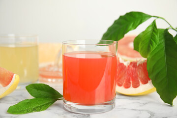 Glass of pink pomelo juice with green leaves on white marble table
