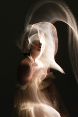 Abstract woman with beige dress and black hairs silhouette in bright light trails of light...