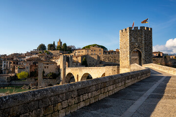 Besalu historic medieval city with Catalonia flags on the stone bridge tower crossing El Fluvia river, in Spain